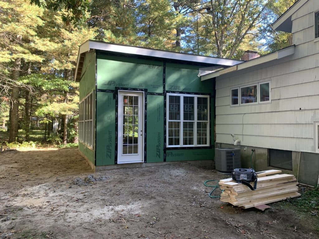 Single-story addition wrapped in green sheathing with new door and windows