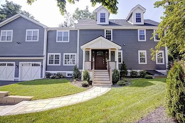 Gray colonial with a covered porch, dormers and carriage-style garage doors